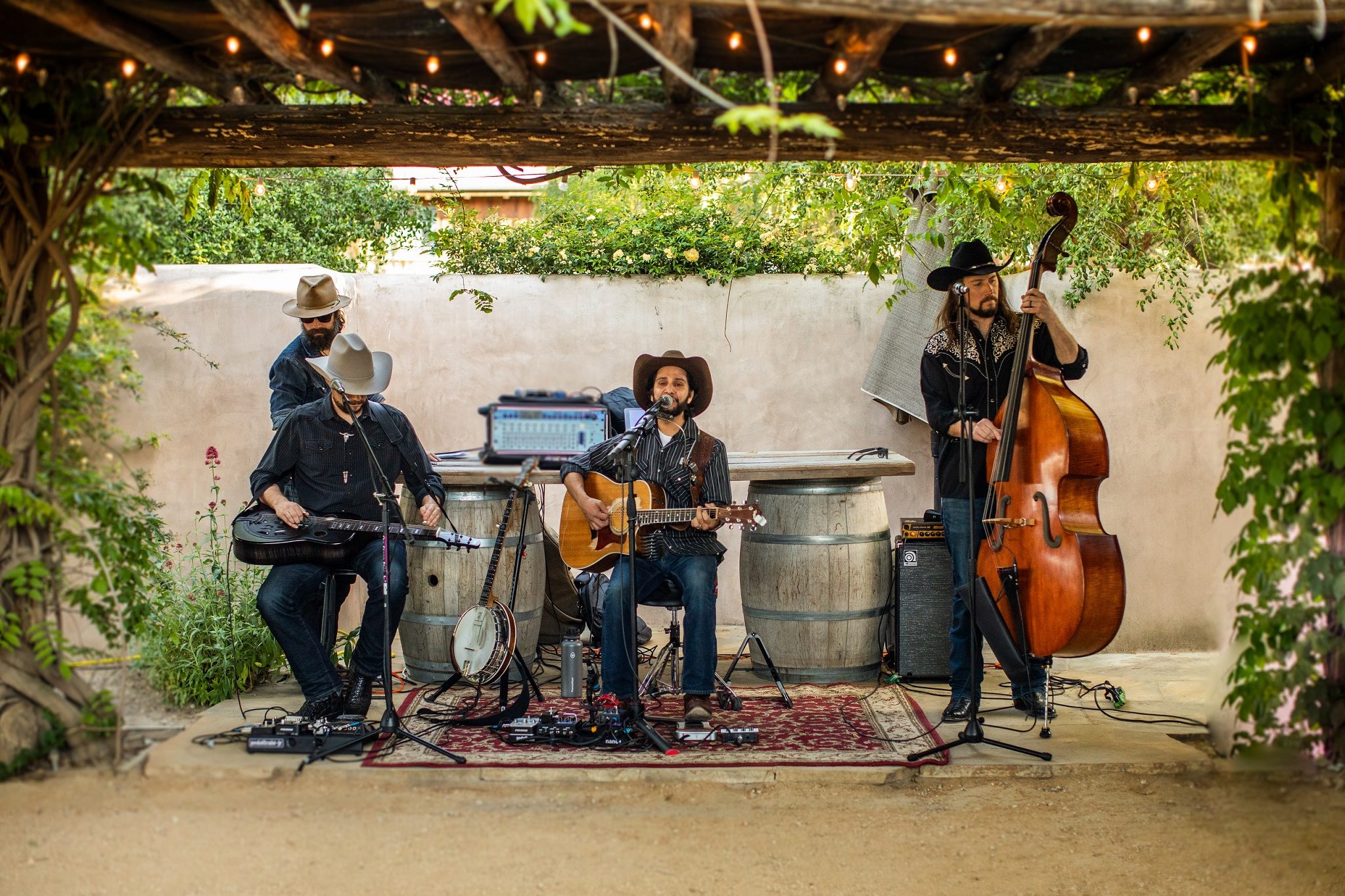 A four-piece band plays in a vine-covered courtyard beside wine barrels