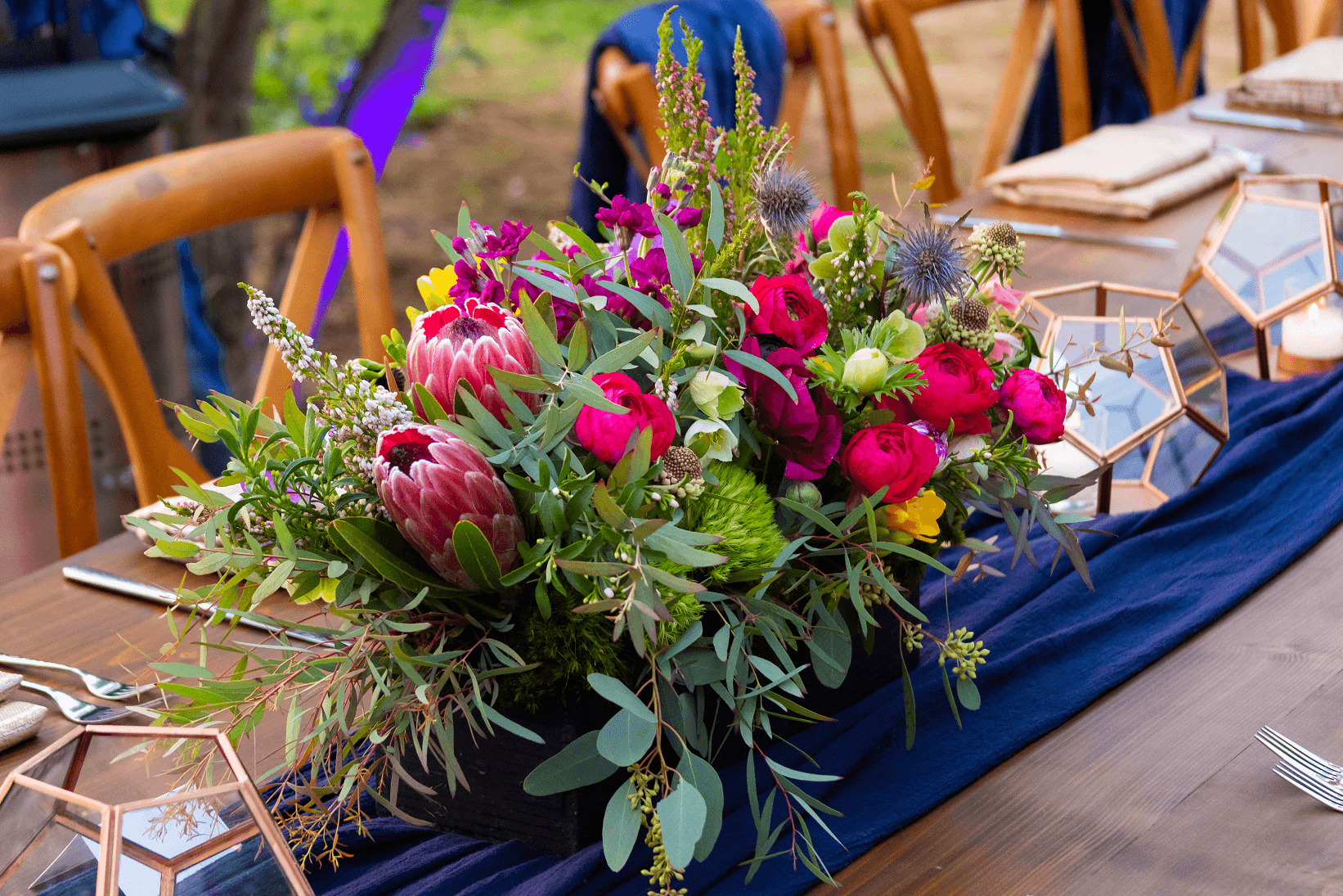 Protea and rose centerpiece on a long table with a navy runner