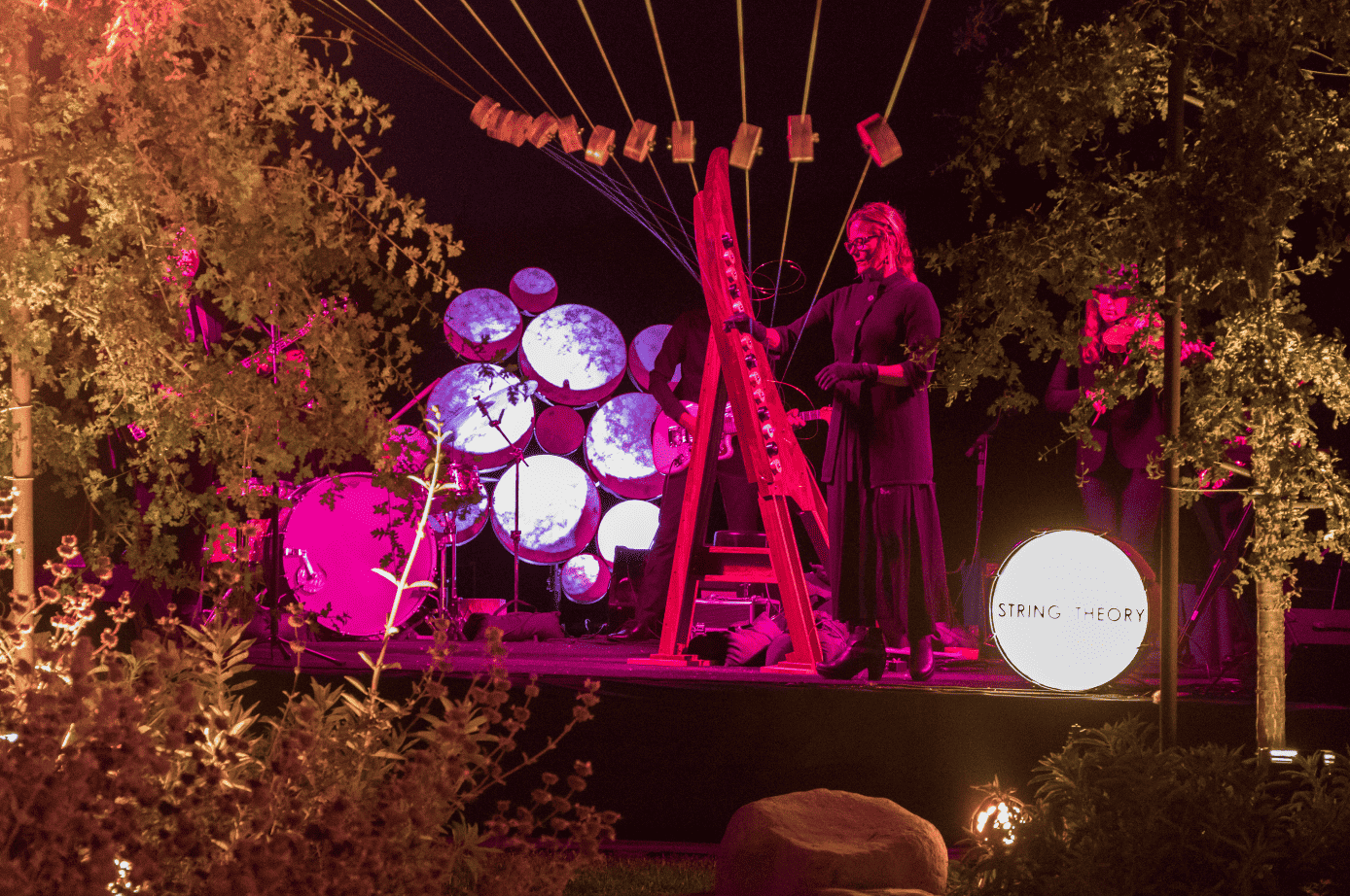Outdoor evening stage lit in pink with a harpist performing